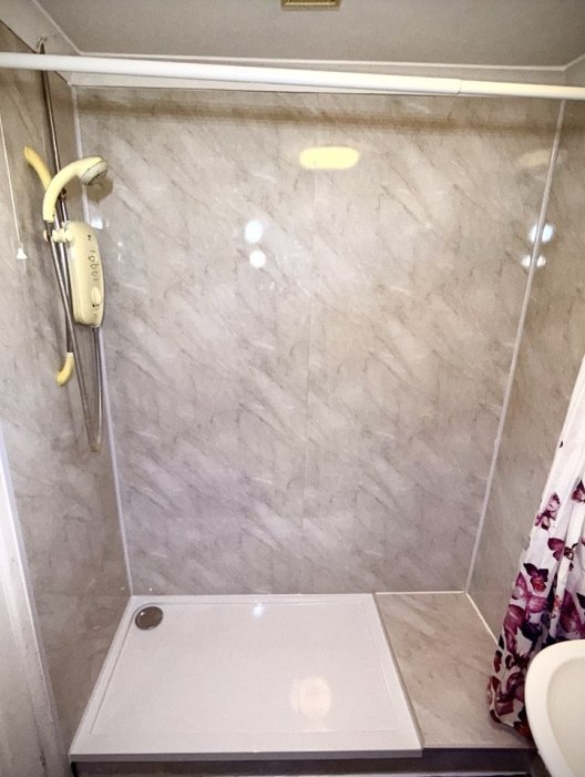 Completed bathroom renovation in Weeley, Essex — old bath replaced with shower tray, wall panels, white silicone sealant, and fully levelled flooring installed by Rez Heating & Plumbing Service