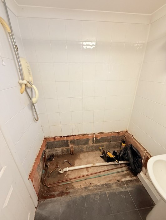 Completed bathroom renovation in Weeley, Essex — old bath replaced with shower tray, wall panels, white silicone sealant, and fully levelled flooring installed by Rez Heating & Plumbing Service